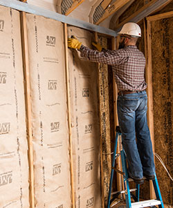 Man on a ladder installing fiberglass batt wall insulation.