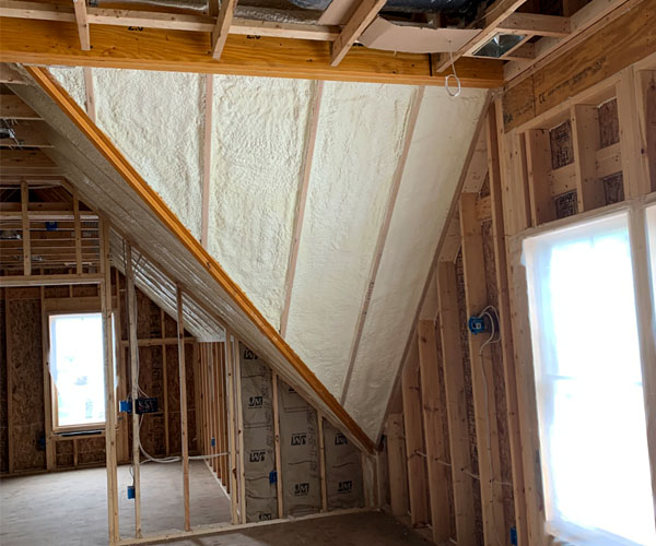 Sloped attic knee wall insulated with spray foam, with fiberglass batt insulation below and exposed wooden framing throughout an unfinished residential space.