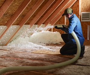 worker spraying foam insulation inside an attic