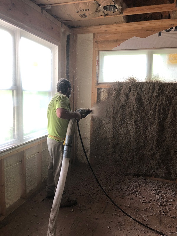 Worker installing wet cellulose insulation in a wall