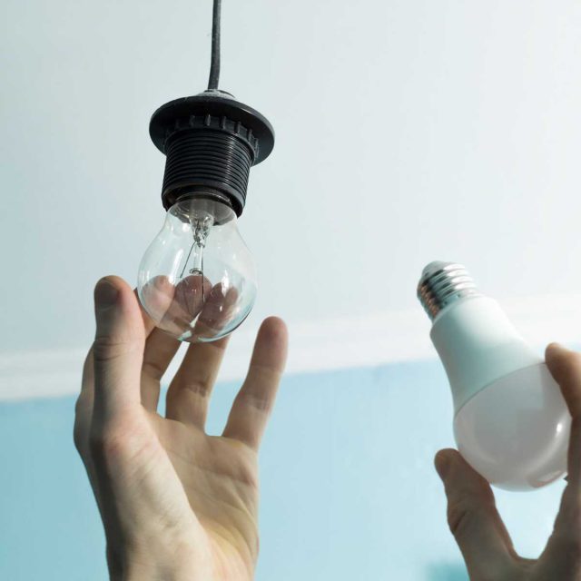 Hands swapping out an incandescent lightbulb with an LED lightbulb.
