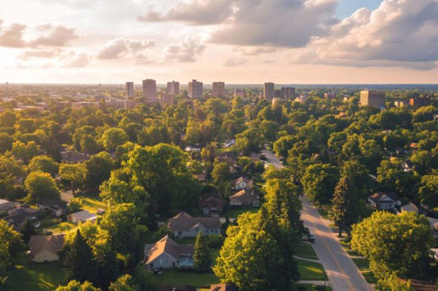 A scenic aerial view of Grand Rapids, Michigan, featuring a mix of suburban homes and a downtown skyline surrounded by lush green trees." Placement Suggestion: At the beginning of the blog, near the introduction.