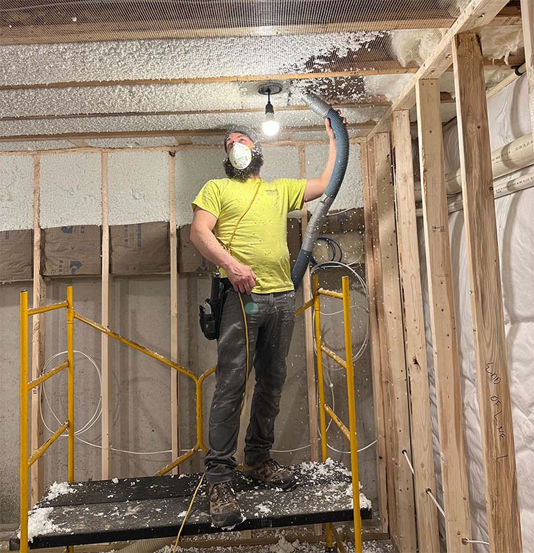 Installer blowing in sound insulation into basement ceiling using netting and loose-fill material.