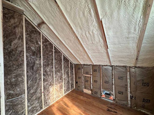 Attic knee wall and sloped ceiling insulated with spray foam and fiberglass batts in a residential remodel.