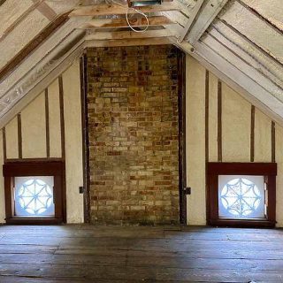 Spray foam insulation installed between attic rafters surrounding two stained-glass windows.