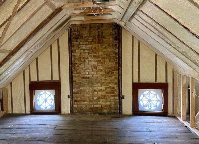 Spray foam insulation installed between attic rafters surrounding two stained-glass windows.