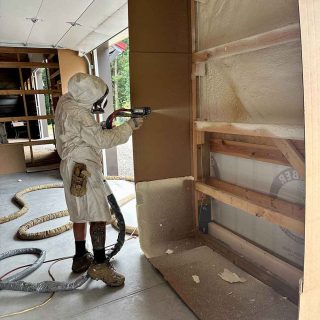 Insulation technician in protective suit spraying foam into open wall framing