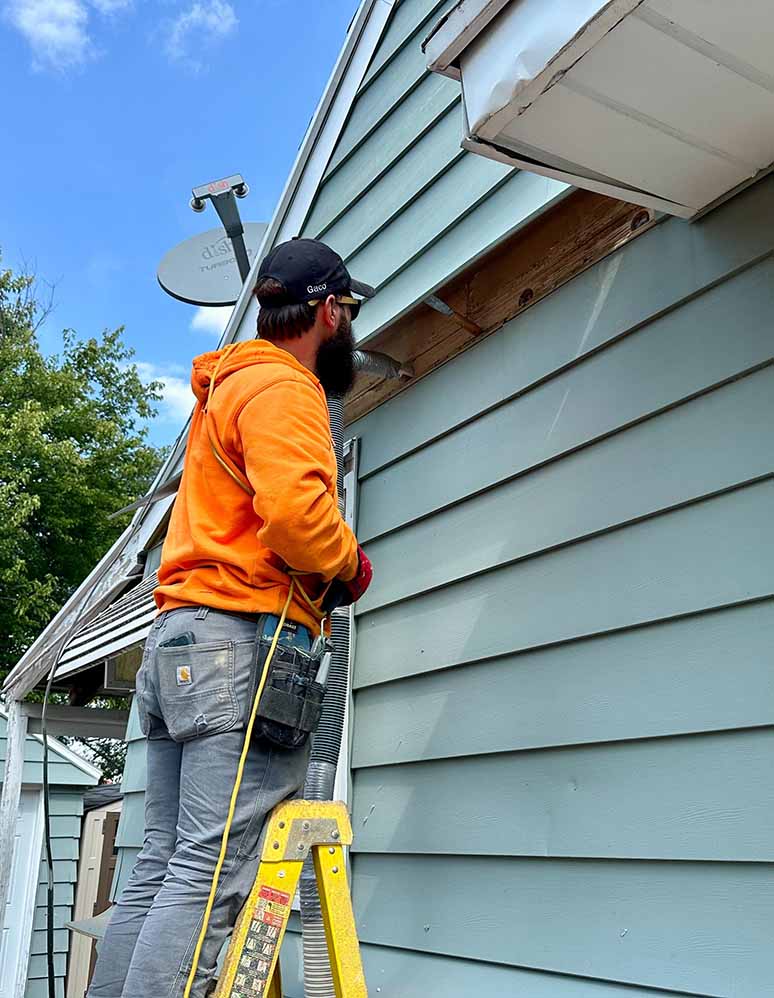 Insulator installing dense-pack cellulose insulation through exterior wall cavities.